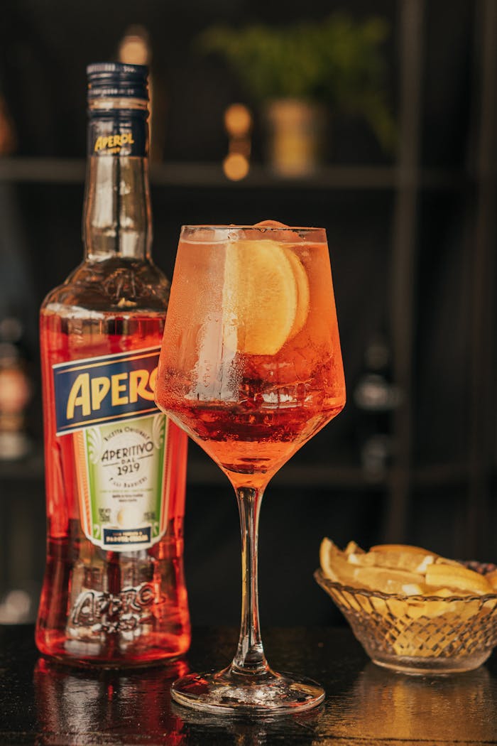 Close-up of a classic Aperol Spritz with orange slice, featuring Aperol bottle and lemon wedges.